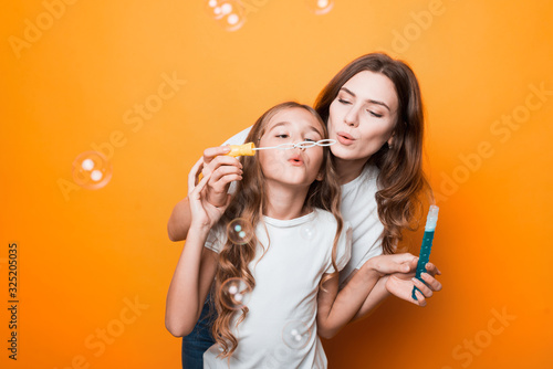 two sisters blow bubbles in studio on orange background