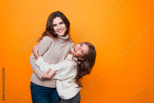two sisters hugging and having fun in studio on orange background. age difference.