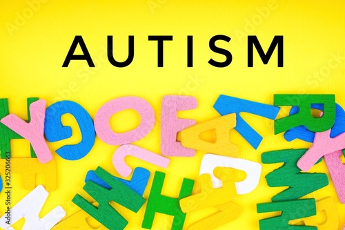 AUTISM  text with ABC wooden letters alphabet scattered on a yellow background. Education and copy space