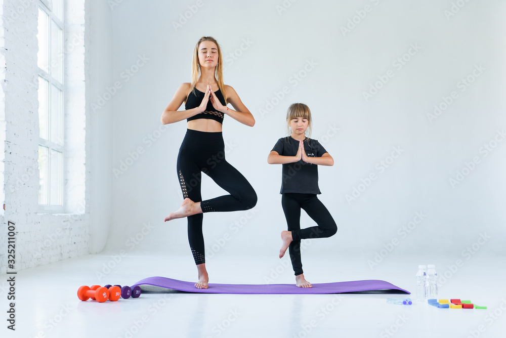 Obraz premium Girl practicing yoga, standing in vrksasana exercise with namaste, tree pose. Female meditation at white loft studio background.