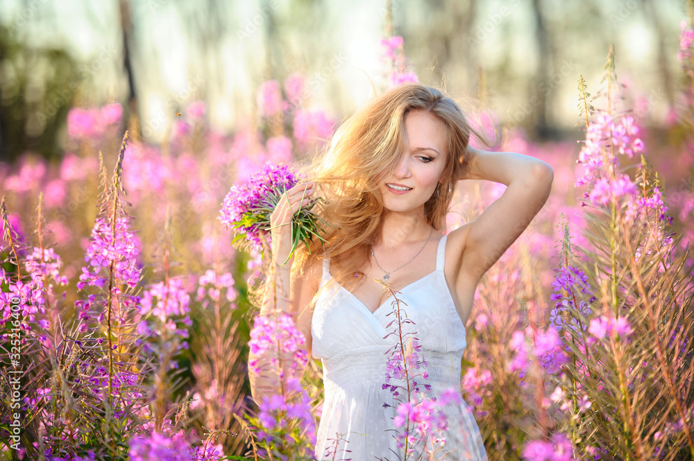 Young beautiful blonde girl gathers pink flowers in the spring blooming field at sunset. Young beautiful blonde girl gathers pink flowers in the spring blooming field at sunset.