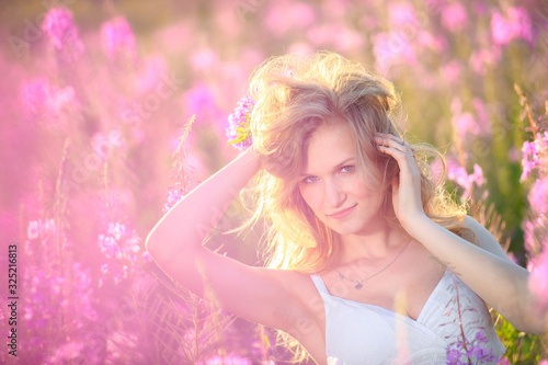 Young beautiful blonde girl gathers pink flowers in the spring blooming field at sunset. © sheikoevgeniya