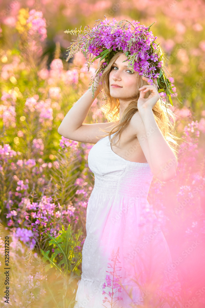 Obraz premium Young beautiful blonde girl gathers pink flowers in the spring blooming field at sunset.