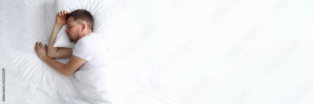 Young caucasian handsome man sleeping on white bed home portrait. Top view background - obrazy, fototapety, plakaty 