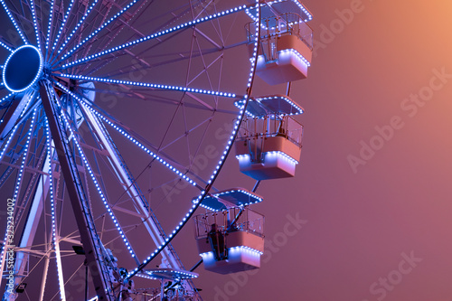 Ferris Wheel illuminated with blue lights on sunset background. Urban Scene. Copy space. Amusement attraction park template