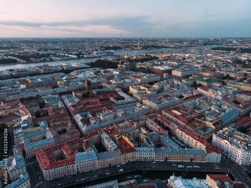Fototapeta premium Aerial view of red and grey rooftops of Saint Petersburg. On the background St. Isaac's Cathedral and Peter and Paul Cathedral. View from above on Moyka river. Evening light. Orthodox church.