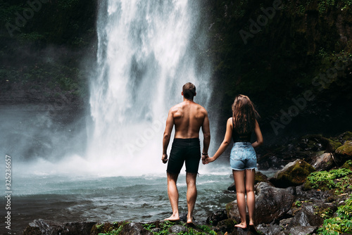 Lovers at the waterfall, rear view. Couple admiring a beautiful waterfall in Indonesia. Couple on vacation in Bali. Honeymoon trip. The couple is traveling in Asia. Vacation on the island of Bali
