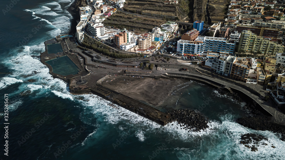 Natural saltwater pools on the Atlantic Ocean in the Canary Islands in Bahamar. Lighthouse. Huge waves crashing on rocks and stone. Shot on a drone from above.