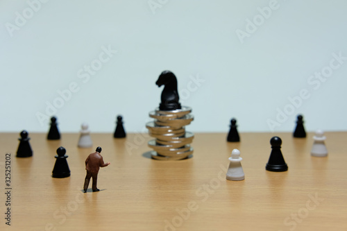 Business strategy conceptual photo - miniature businessman standing in front horse chess piece at coin stack