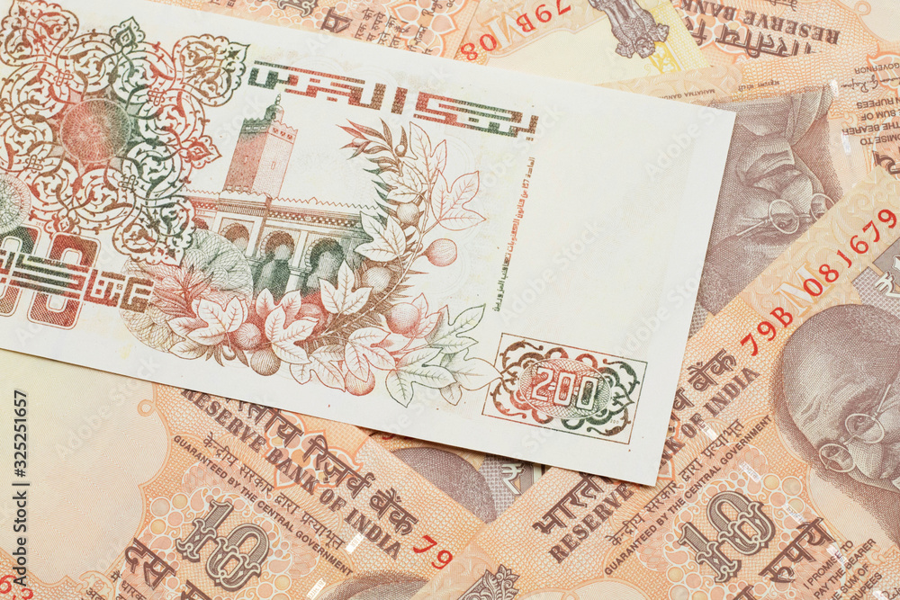 A macro image of a beige two hundred Algerian dinar bank note on a background of Indian ten rupee bank notes