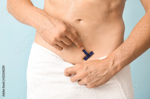 Handsome young man shaving his body on color background, closeup
