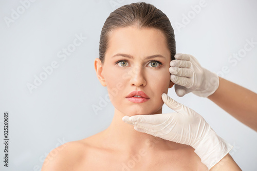 Plastic surgeon touching face of young woman against light background