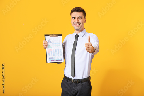 Male bank manager with document showing thumb-up gesture on color background