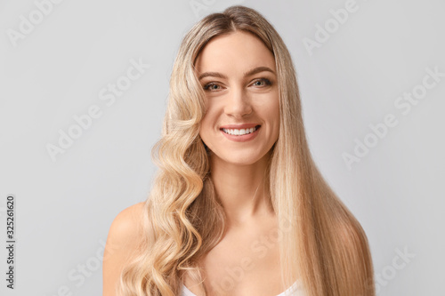 Beautiful young woman with curly and straight hair on light background