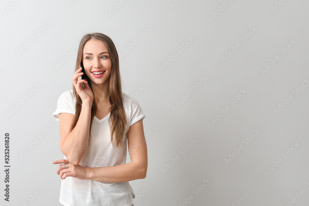 Young woman talking by mobile phone on light background Young woman talking by mobile phone on light background