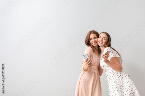 Young women with mobile phones on light background