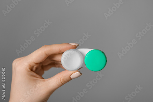 Female hand holding container with contact lenses on grey background