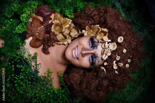 Woman decorating with fantasy green grass big hair mashrooms and make up with long eyeslashes smiling on background. photo