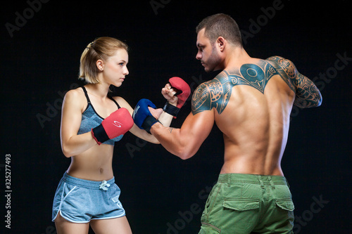 Young muscular woman and man in boxing gloves practicing isolated on black © satyrenko