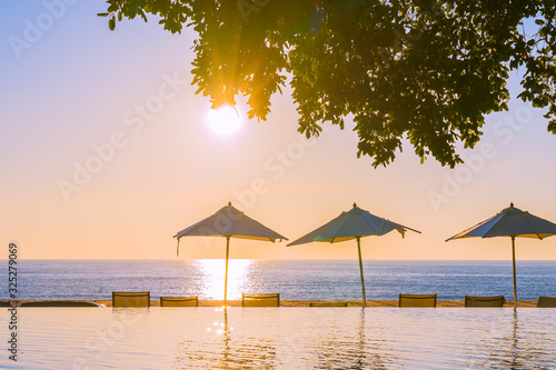 Beautiful tropical outdoor beach sea ocean with umbrella and chiar around outdoor swimming pool at sunset or sunrise time © siraphol