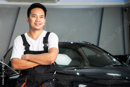 A Car Wrapping Specialist wearing car service costume standing and cross one's arm with the black car in the background. Auto car repair service center. Professional service. © artitwpd