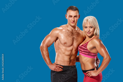 Beautiful couple of muscular fit man and woman bodybuilder hugging on azure shade blue background