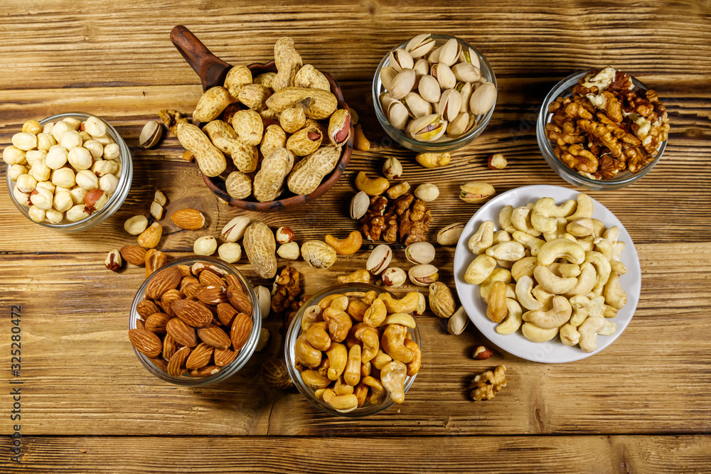 Assortment of nuts on wooden table. Almond, hazelnut, pistachio, peanut, walnut and cashew in small bowls. Top view. Healthy eating concept Assortment of nuts on wooden table. Almond, hazelnut, pistachio, peanut, walnut and cashew in small bowls. Top view. Healthy eating concept
