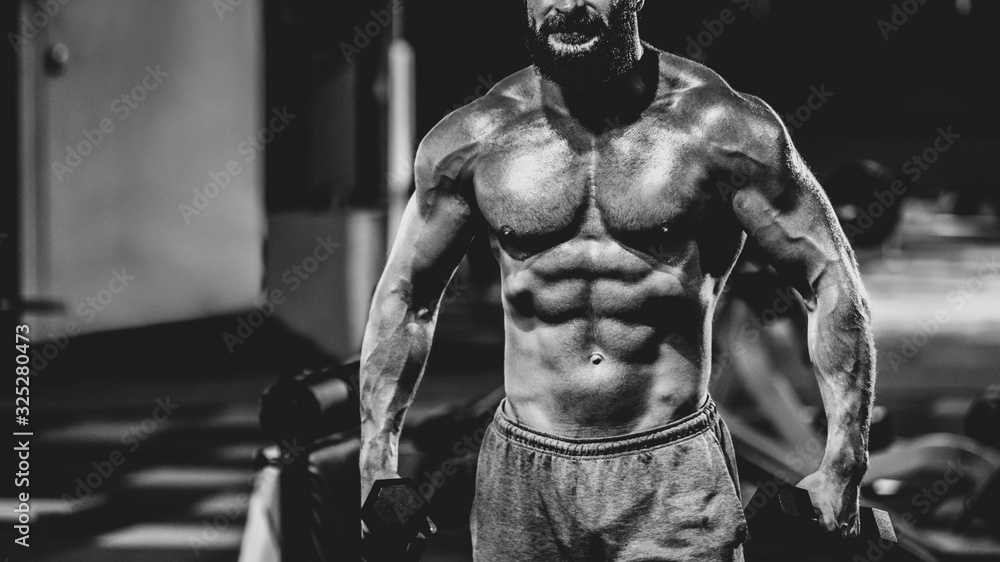 Handsome man with perfect muscular body training hard in gym, dramatic black and white image