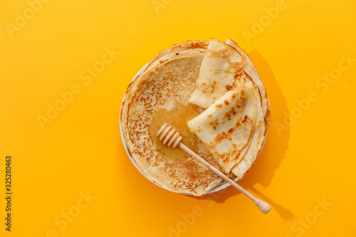 Delicious homemade pancakes with honey on a yellow background. Top view, close-up. Traditional holiday celebration concept. Russian translation wide and happy Shrovetide Maslenitsa.