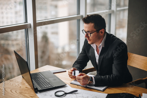 accountant guy looks at a laptop and holds a credit card in his hands