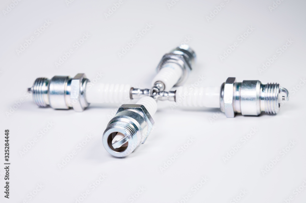 Obraz premium Subject shooting on a gray background. new four spark plugs, spare parts for a gasoline engine. The concept of new auto parts and maintenance