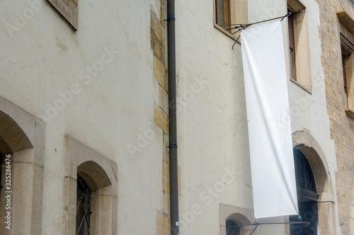 Light wall of an old building with a white blank vertical banner for an inscription or advertising image
