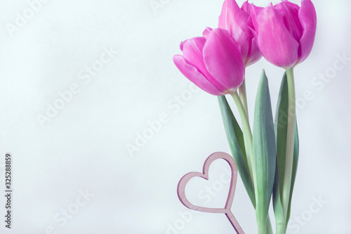 A bouquet of three crimson tulips and a wooden heart. Greeting card concept