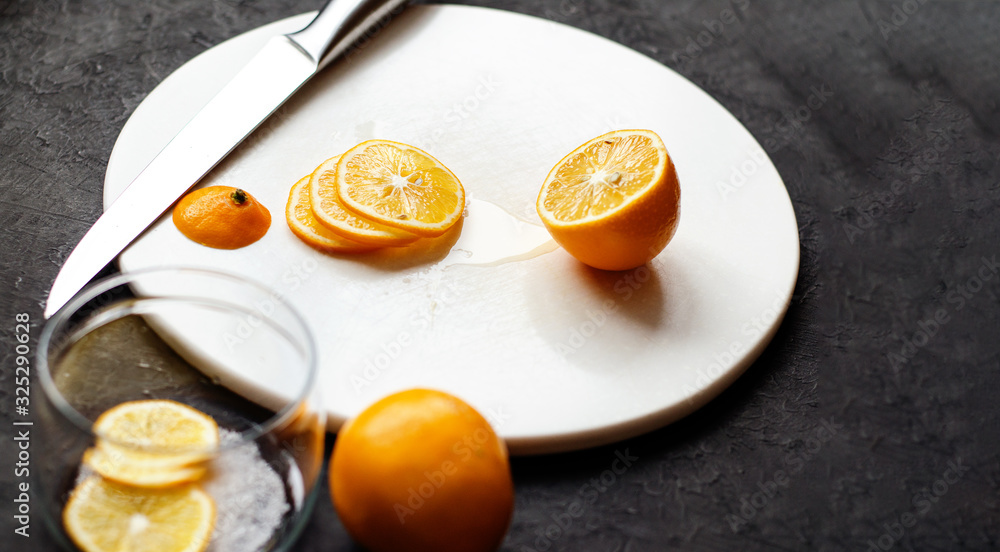 Dark moody. Food black background. On a white stone board in the hands of a girl, a knife cuts a lemon. Slices of lemon are piled in a glass jar and sprinkled with sugar. Dark moody. Food black background. On a white stone board in the hands of a girl, a knife cuts a lemon. Slices of lemon are piled in a glass jar and sprinkled with sugar.