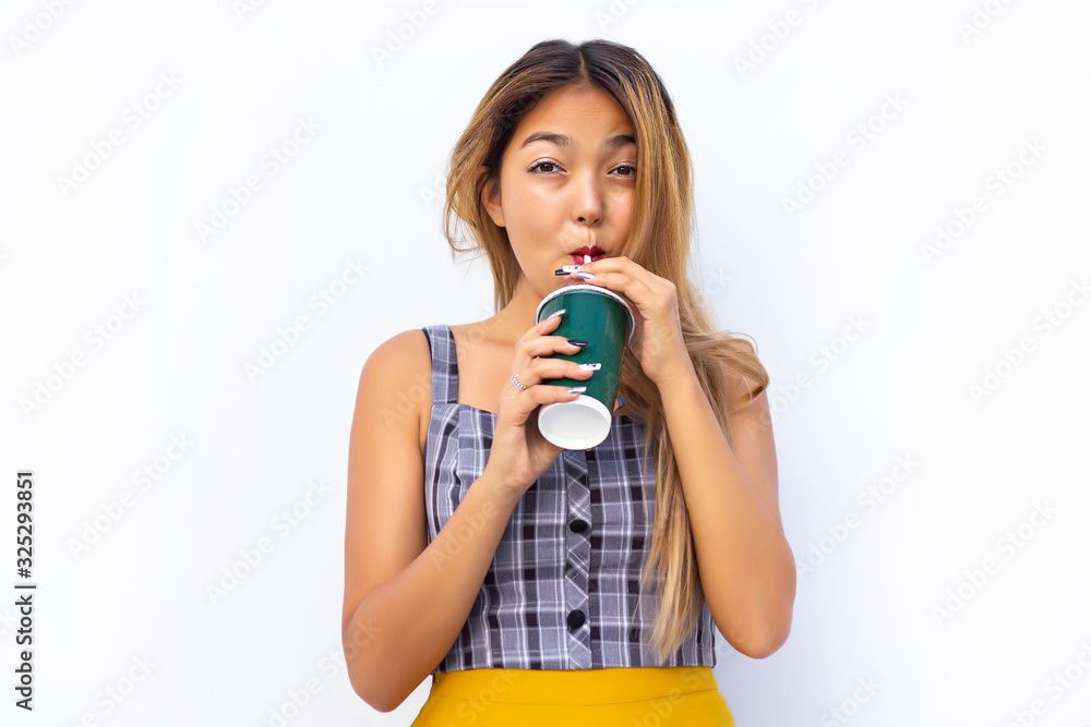 Happy smiling woman holding a glass of coffee (to go) in her hands, drinking a drink through a straw. The girl laughs and smiles, looking directly at the camera on an isolated background Happy smiling woman holding a glass of coffee (to go) in her hands, drinking a drink through a straw. The girl laughs and smiles, looking directly at the camera on an isolated background