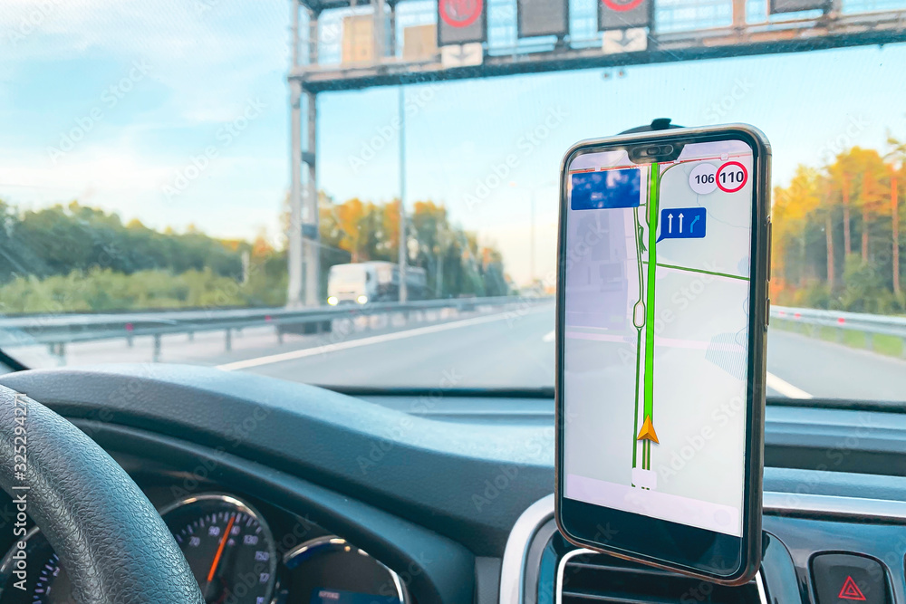 Fototapeta premium The smartphone in the car is used for navigation or GPS. The movement of the car with a smartphone in the holder. Mobile phone isolated white screen. Copy spaces. Vehicle interior.