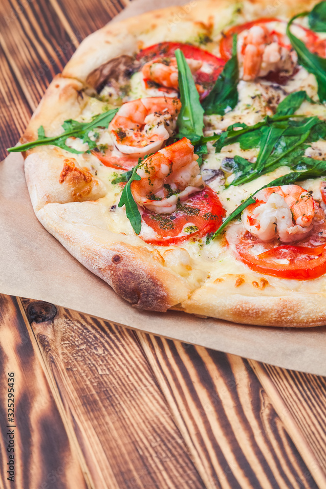 slice of italian pizza with royal prawns, tomatoes, cheese and arugula on a classic dough on a wooden table close-up