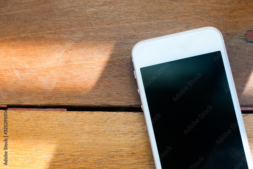 A smart phone with turned-off display placed on a brown wooden table A smart phone with turned-off display placed on a brown wooden table