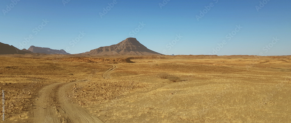 Road across a desert landscape with background mountain in Namibia