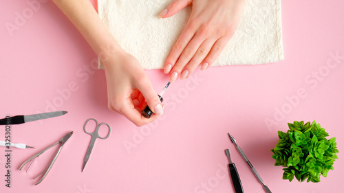 Woman performing a manicure on herself. Female hands with nail polish, manicure and pedicure tools on pink background, view from above. Self-care beauty treatment concept
