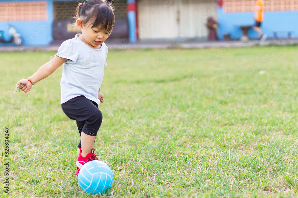 Happy Asian baby child girl playing and kicking a ball toys at the field playground. She smiling and wearing a blue shirt. Baby aged of 1-2 years old. Exercise for health. Sport and kids concept. Happy Asian baby child girl playing and kicking a ball toys at the field playground. She smiling and wearing a blue shirt. Baby aged of 1-2 years old. Exercise for health. Sport and kids concept.