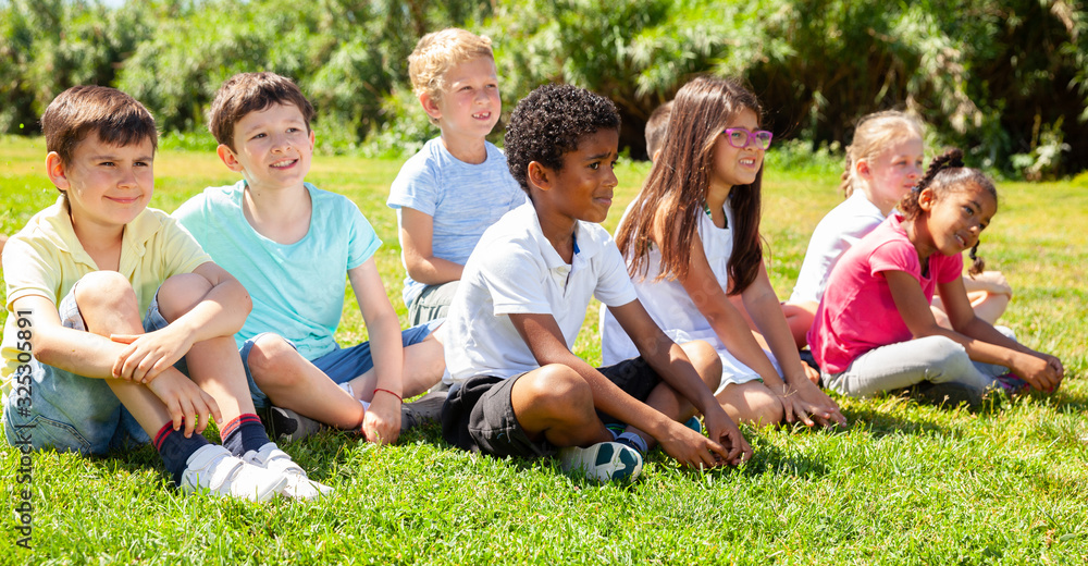 Fototapeta premium Team of friends children resting on grass together in park