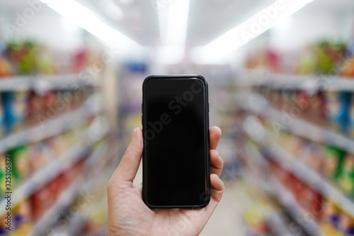 A close up of a man holding a modern smartphone at a supermarket with a blank screen for text or background design