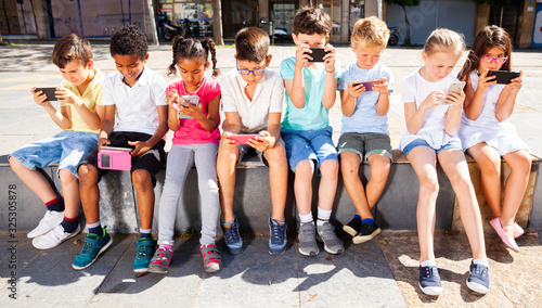 Children using mobile devices  outdoors at sunny day