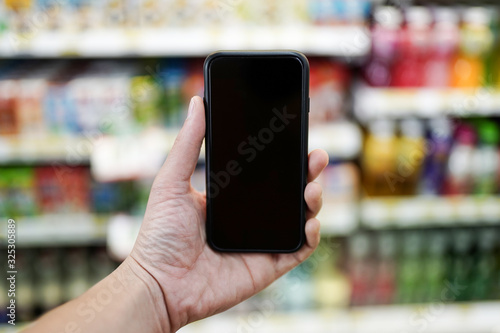 A close up of a man holding a modern smartphone at a supermarket with a blank screen for text or background design
