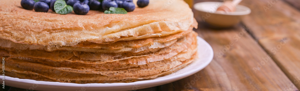 Pancakes with blueberries and honey on a plate, on wooden roofing. Traditional pastries for the Russian festival of Maslenitsa. free space for text. Pancakes with blueberries and honey on a plate, on wooden roofing. Traditional pastries for the Russian festival of Maslenitsa. free space for text.