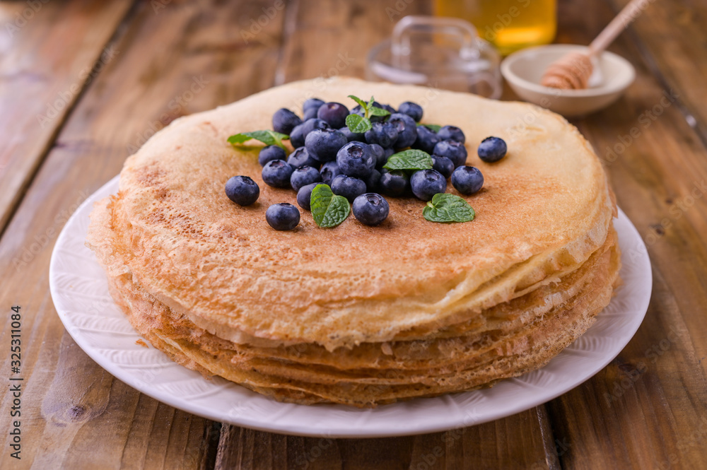 Pancakes with blueberries and honey on a plate, on wooden roofing. Traditional pastries for the Russian festival of Maslenitsa. free space for text. Pancakes with blueberries and honey on a plate, on wooden roofing. Traditional pastries for the Russian festival of Maslenitsa. free space for text.