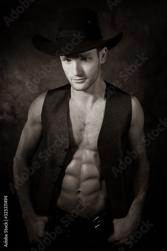 Portrait of handsome cowboy looking at camera wearing hat with open waistcoat revealing defined pecs and sixpack abs