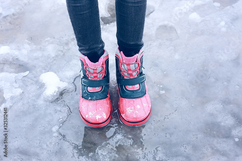 winter children s boots   rubber bright children s shoes on the street  baby s feet in shoe slush  snowfall  puddles. Cold weather  ice  snow  rain. Walking in bad weather