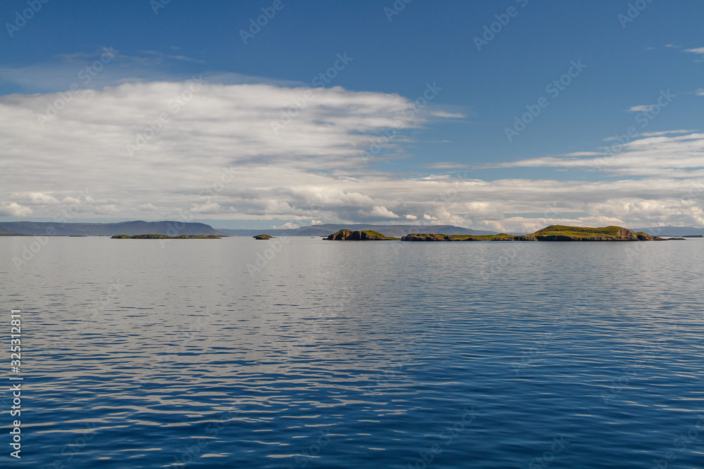 Die Inselgruppe der Flatey Inseln vor Island an einem sonnigen Tag mit spiegelglatter Meeresoberfläche unter blauem Himmel